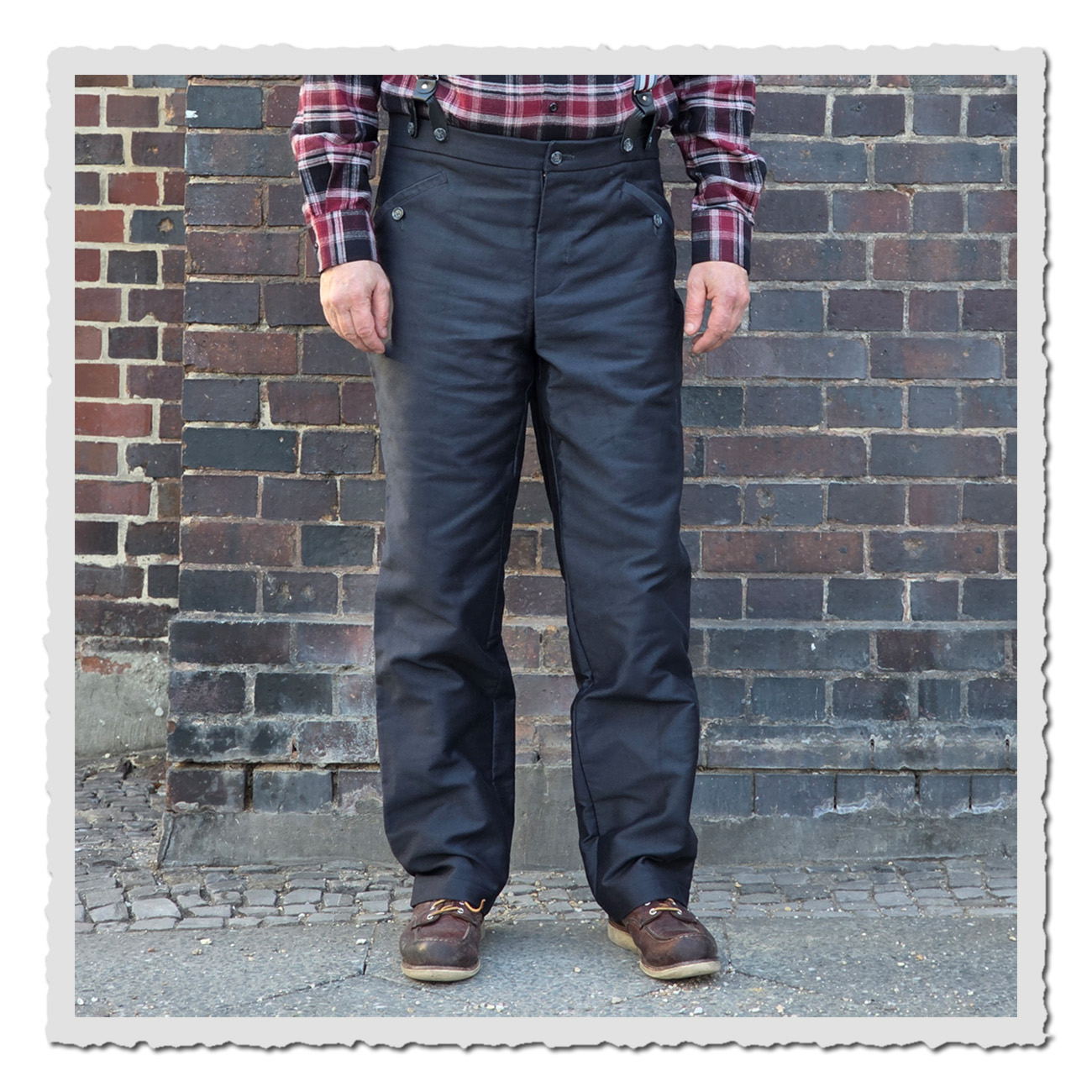 Arbeiterhose Gustav I in Anthrazit, hohe Leibhöhe und Cinch-Back, getragen im Vintage-Workwear-Look vor Ziegelwand.